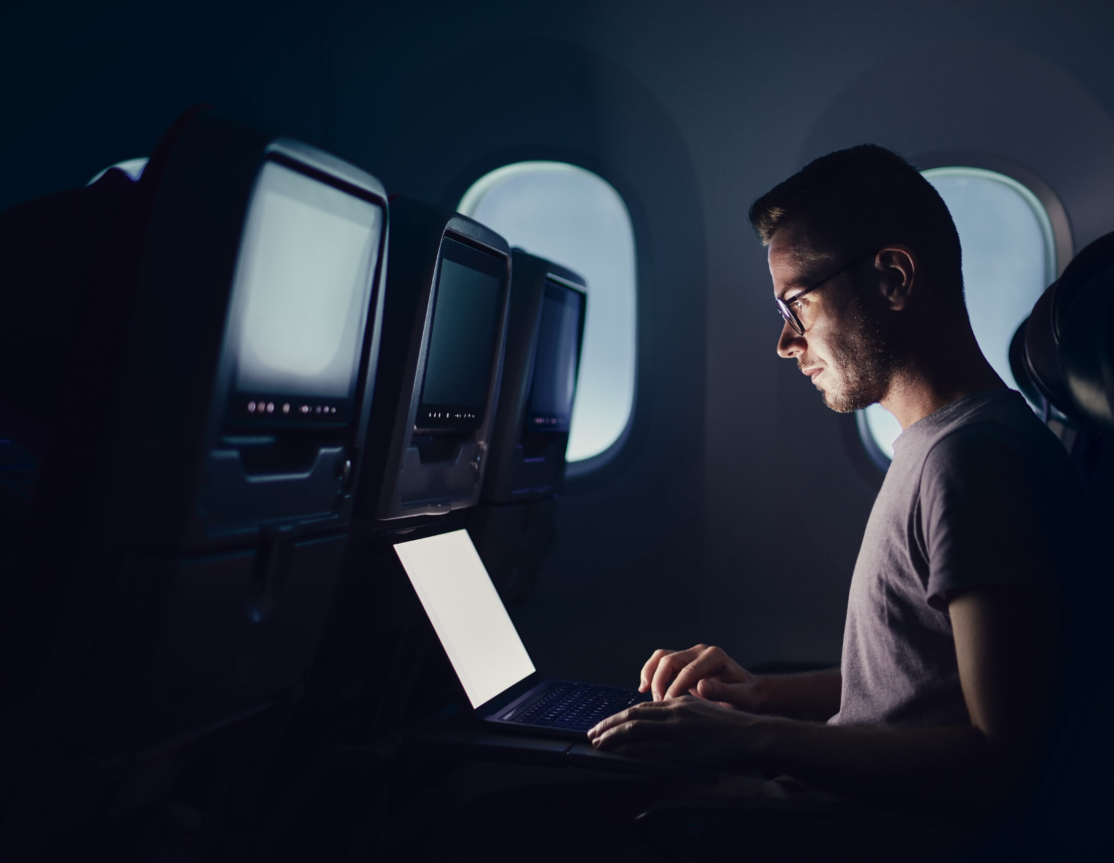 Man traveling by airplane. Young passenger using laptop during night flight.