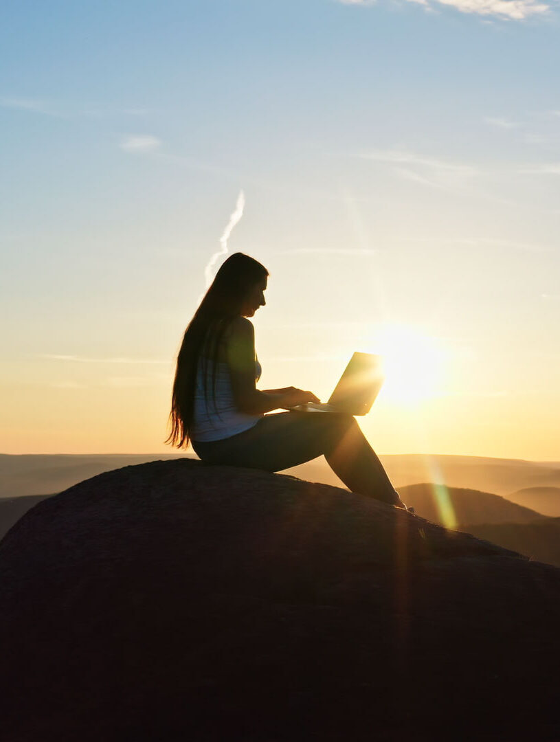 Female traveller sitting on a hill and using a laptop in holidays